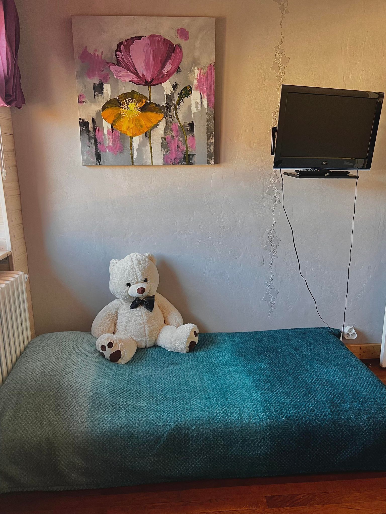 Una habitación con una cama, un osito de peluche, un cuadro y un televisor.