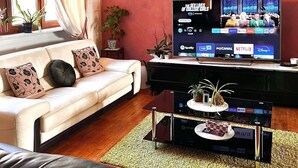 Un soggiorno moderno con un divano bianco, un mobile TV nero e una televisione che mostra l'interfaccia di un servizio di streaming.