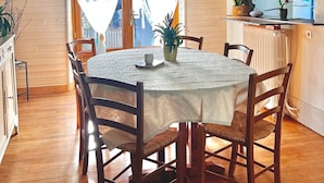 Un'area pranzo con un tavolo rotondo, sei sedie, una tovaglia bianca e un lampadario.