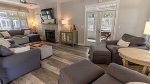 Ein Wohnzimmer mit Kamin, grauen Sofas, einem Couchtisch und einem über dem Kamin montierten Fernseher.