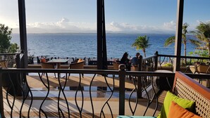 Un espace extérieur aménagé avec des tables et des chaises, offrant une vue sur un plan d’eau et des montagnes au loin.