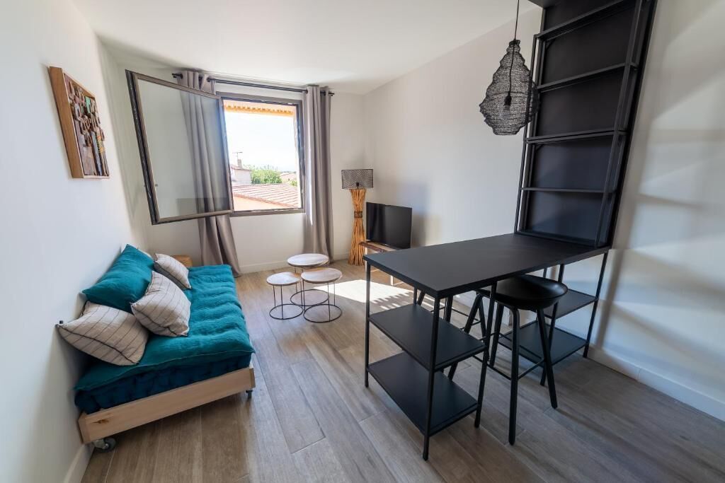 A compact living space with a bed, a dining table with chairs, a TV, and a large window.
