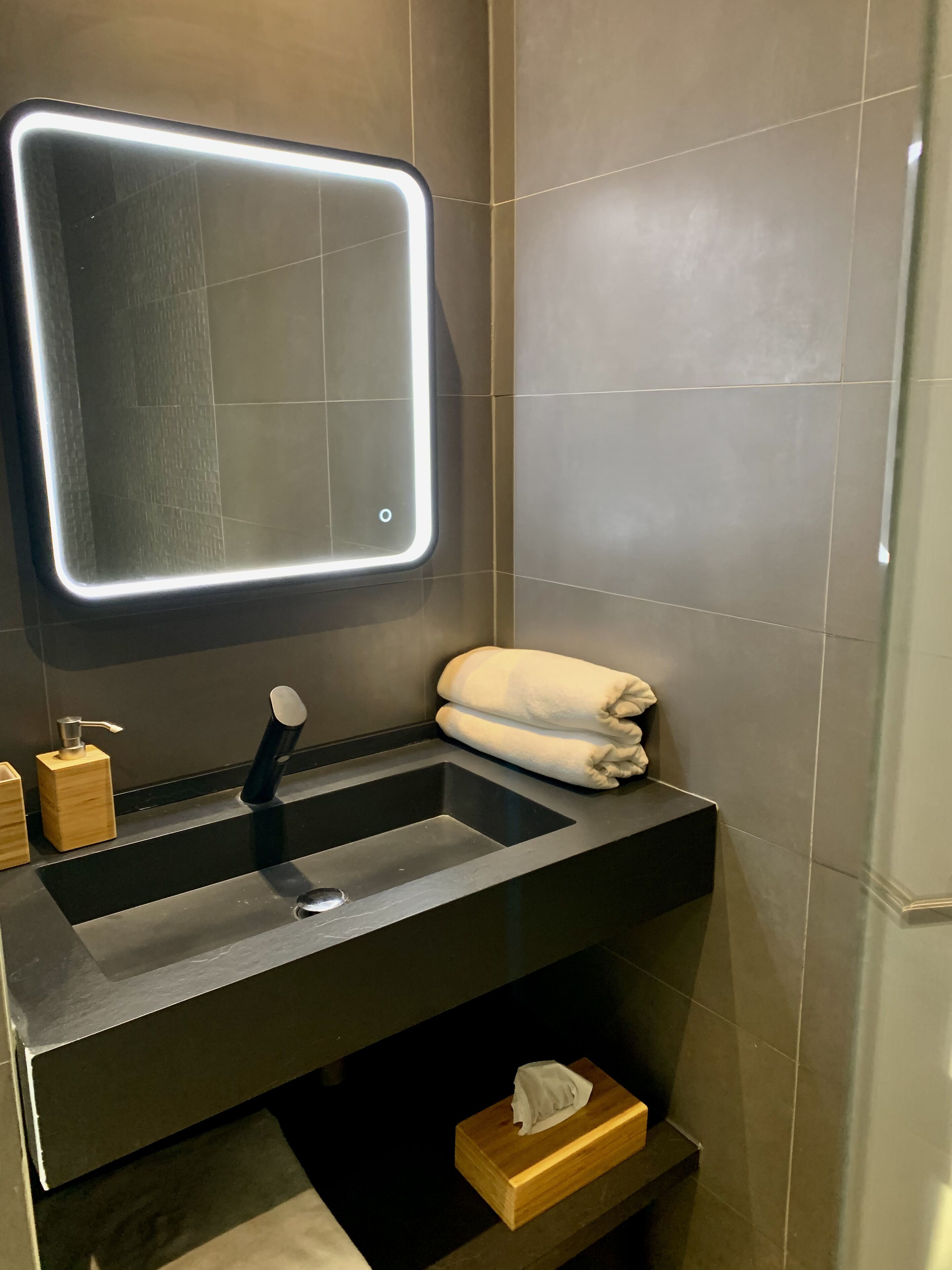 Un baño moderno con un lavabo negro, un espejo con luz y un perchero para toallas.