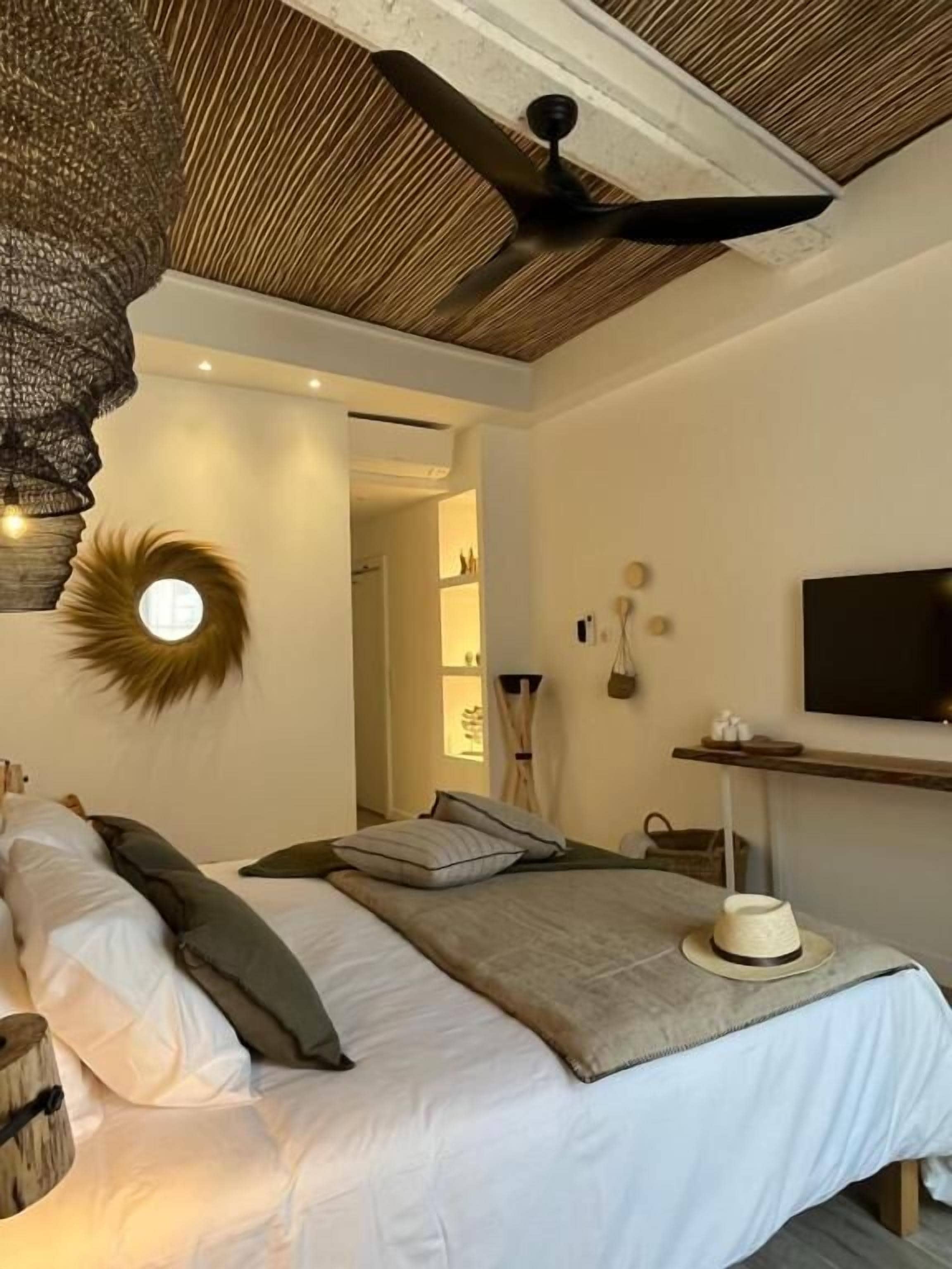 Un dormitorio con cama, ventilador de techo, televisor montado en la pared y espejo circular.