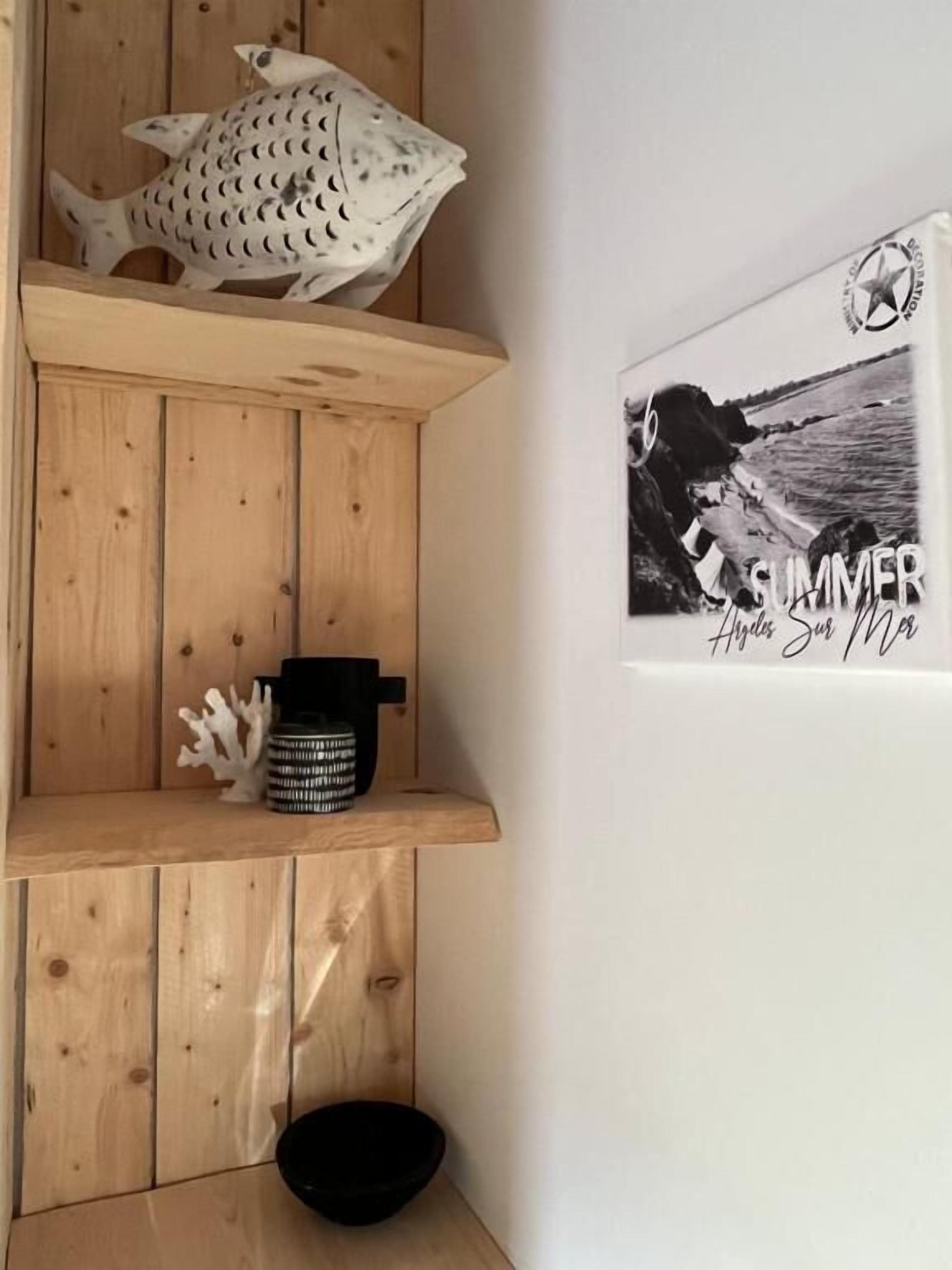 Une étagère en bois ornée d’un poisson décoratif, d’un bol noir et d’une photographie encadrée représentant une scène de plage.