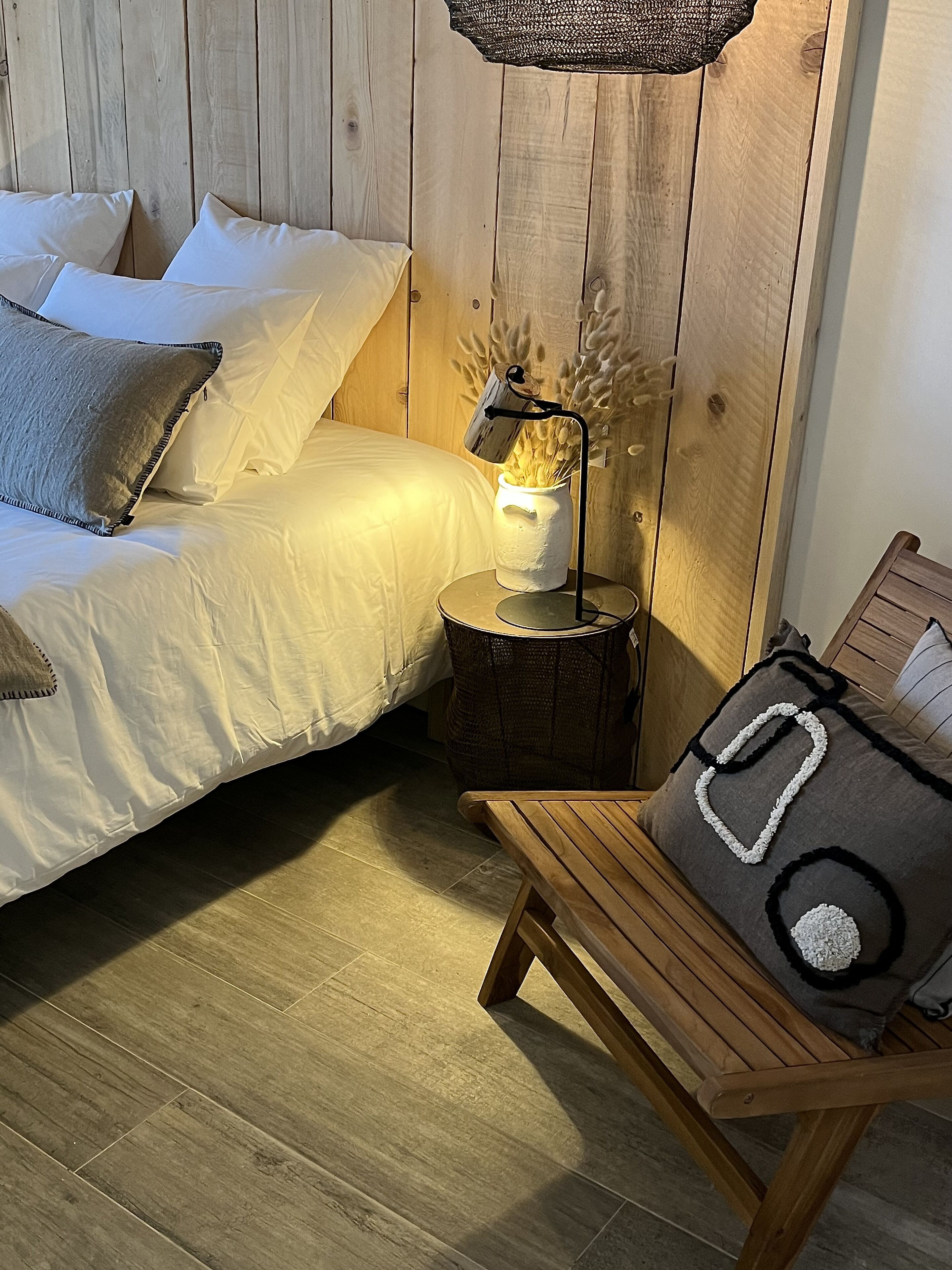 Une chambre confortable avec une tête de lit en bois, une table de chevet avec une lampe, un banc et un lit avec des oreillers.