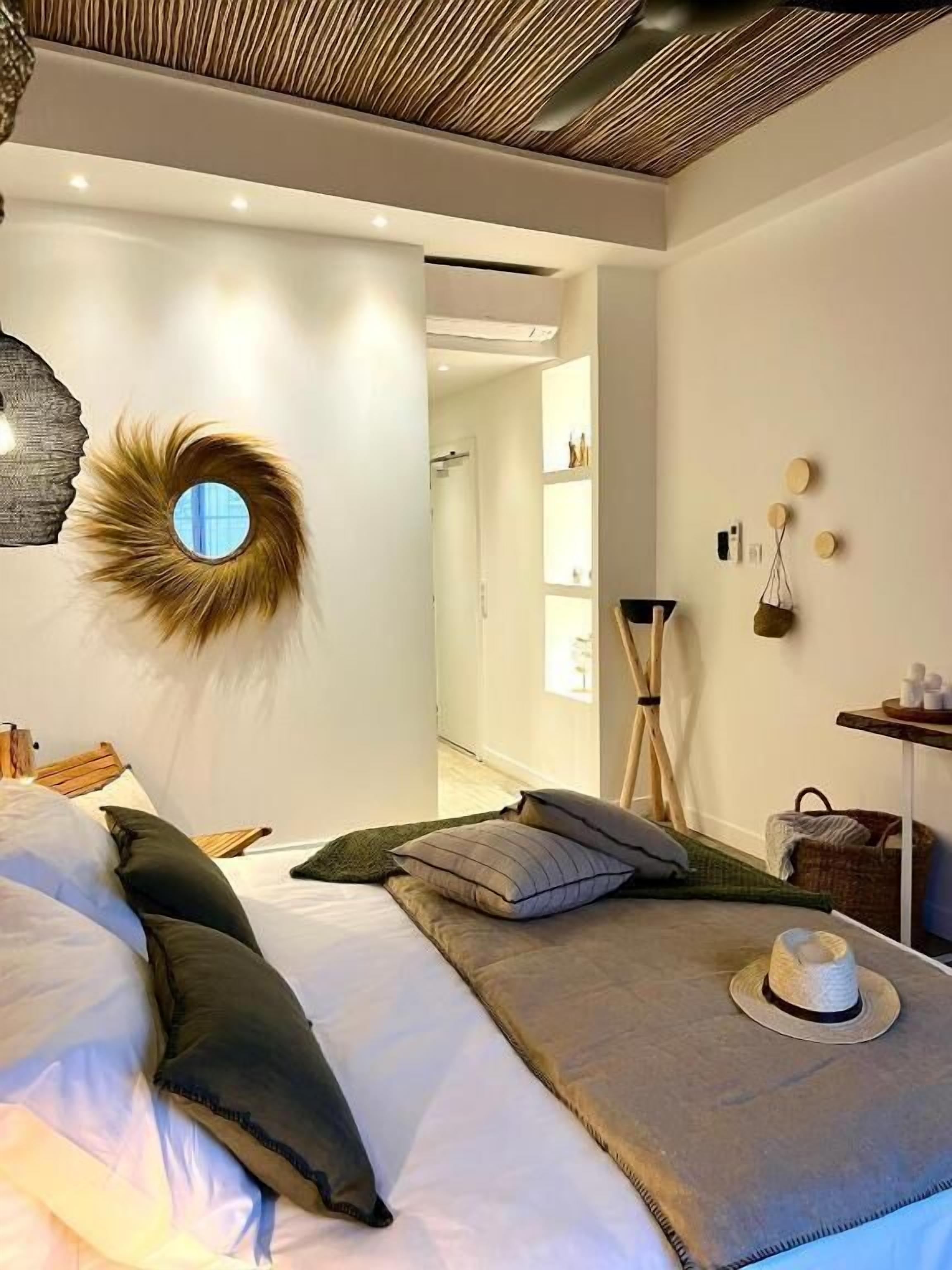 Um quarto moderno com uma cama, almofadas, um chapéu e um espelho fixado na parede.