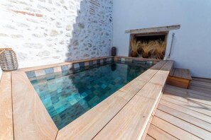 Una piscina moderna al aire libre con un muro de piedra de fondo, una terraza de madera y una chimenea rústica.