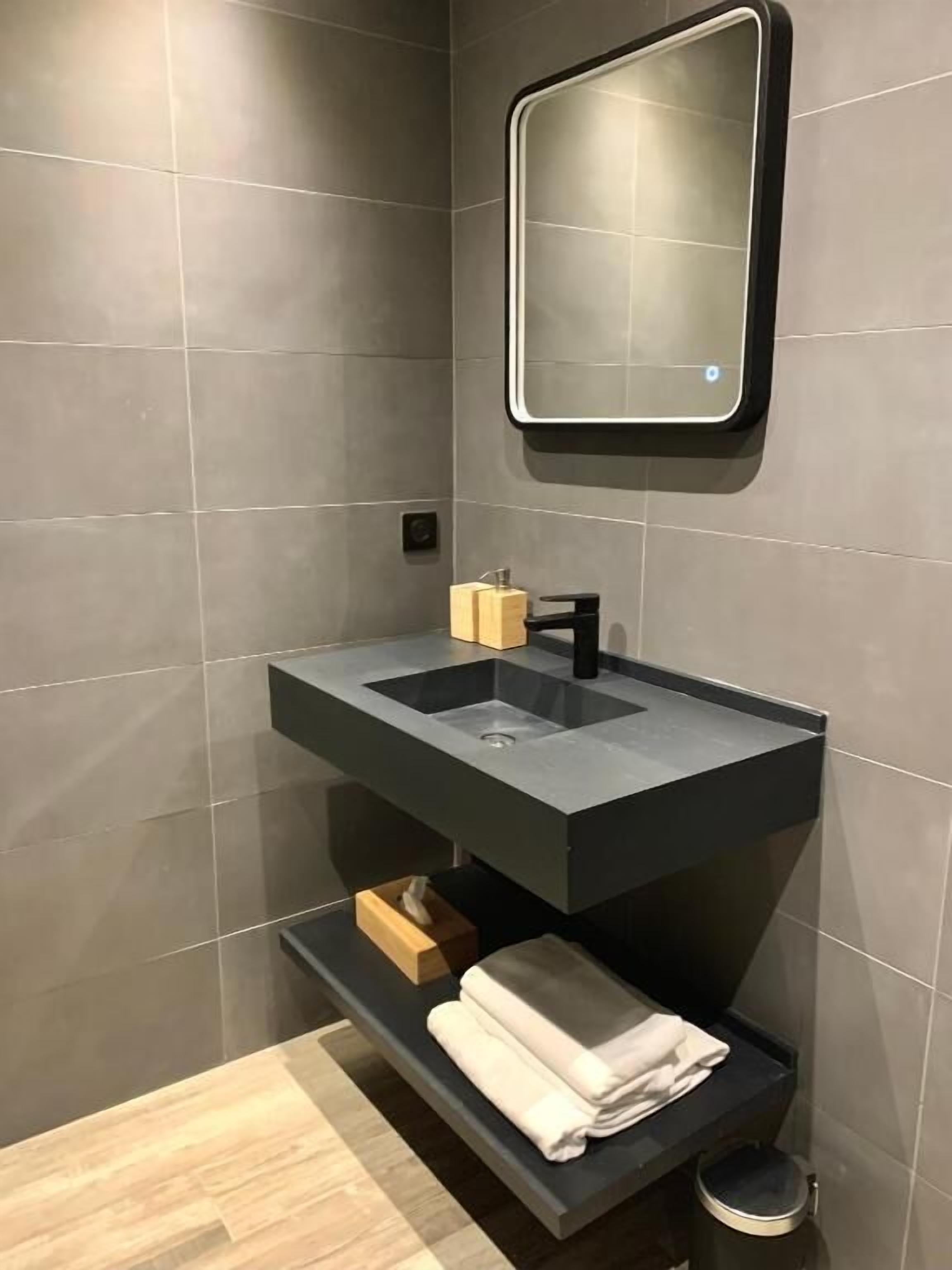 Un baño moderno con un lavamanos oscuro, un espejo y un perchero para toallas.
