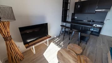 Een moderne woonkamer met een flatscreen televisie, een houten salontafel en een eethoek met krukken.