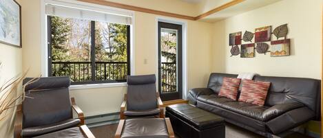A living room with a black leather sofa, two armchairs, a coffee table, and a door leading outside.