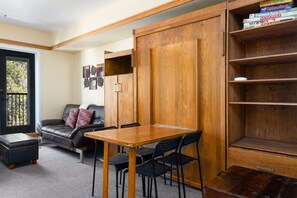 A compact living space with a wooden cabinet, a black leather sofa, a wooden dining table with chairs, and a small ottoman. - 2767 Slopeside Condo by RedAwning (Keystone)