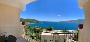 A balcony with a view of the sea, a table with a vase of flowers, and a railing. - Fedra Apartments (Poros)