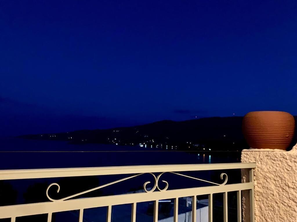 Un balcón con barandilla que da a una masa de agua y un paisaje urbano distante de noche.