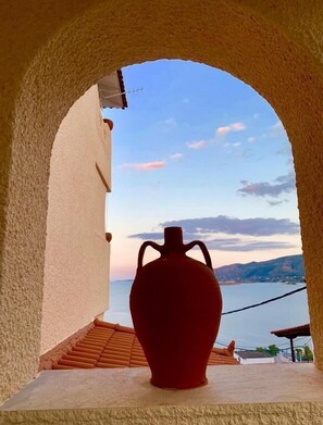 A large red vase on a balcony with a view of the sea and mountains.