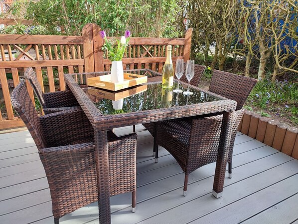 Un juego de comedor exterior de mimbre con una mesa y sillas de vidrio, una botella de vino y dos copas de vino en una terraza.
