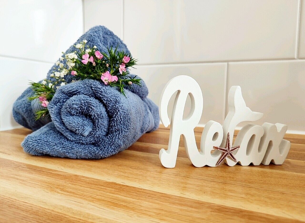 A rolled blue towel with pink flowers on a wooden surface next to a white sign with the word "Retreat" and a star.