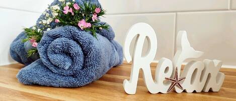 Een opgerolde blauwe handdoek met roze bloemen op een houten oppervlak, naast een wit bord met de tekst 'Retreat' en een ster.