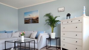 A living room with a grey sofa, a coffee table, a potted plant, a dresser, and a painting on the wall.