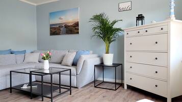 Ein Wohnzimmer mit grauem Sofa, einem Couchtisch, einer Zimmerpflanze, einer Kommode und einem Bild an der Wand.