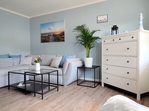 Una sala de estar con un sofá gris, una mesa de centro, una planta en maceta, un aparador y un cuadro en la pared.