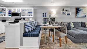 A modern kitchen with white cabinetry, a dining area with a bench, and a grey sofa. - Charming 2 Bed 2 Bath True Blue Pawleys Island Golf, 4 Pools Beach 5 min drive! (Pawleys Island)