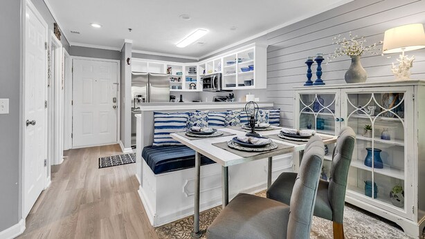 A modern kitchen with white cabinetry, a dining area with a table set for four, and a built-in bench with blue cushions. - Charming 2 Bed 2 Bath True Blue Pawleys Island Golf, 4 Pools Beach 5 min drive! (Pawleys Island)