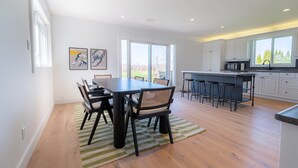 Una cocina moderna con armarios blancos, una isla central con taburetes y una zona de comedor con mesa y sillas.