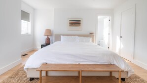 Un dormitorio minimalista con una cama grande, una mesita de noche con lámpara y un cuadro en la pared.