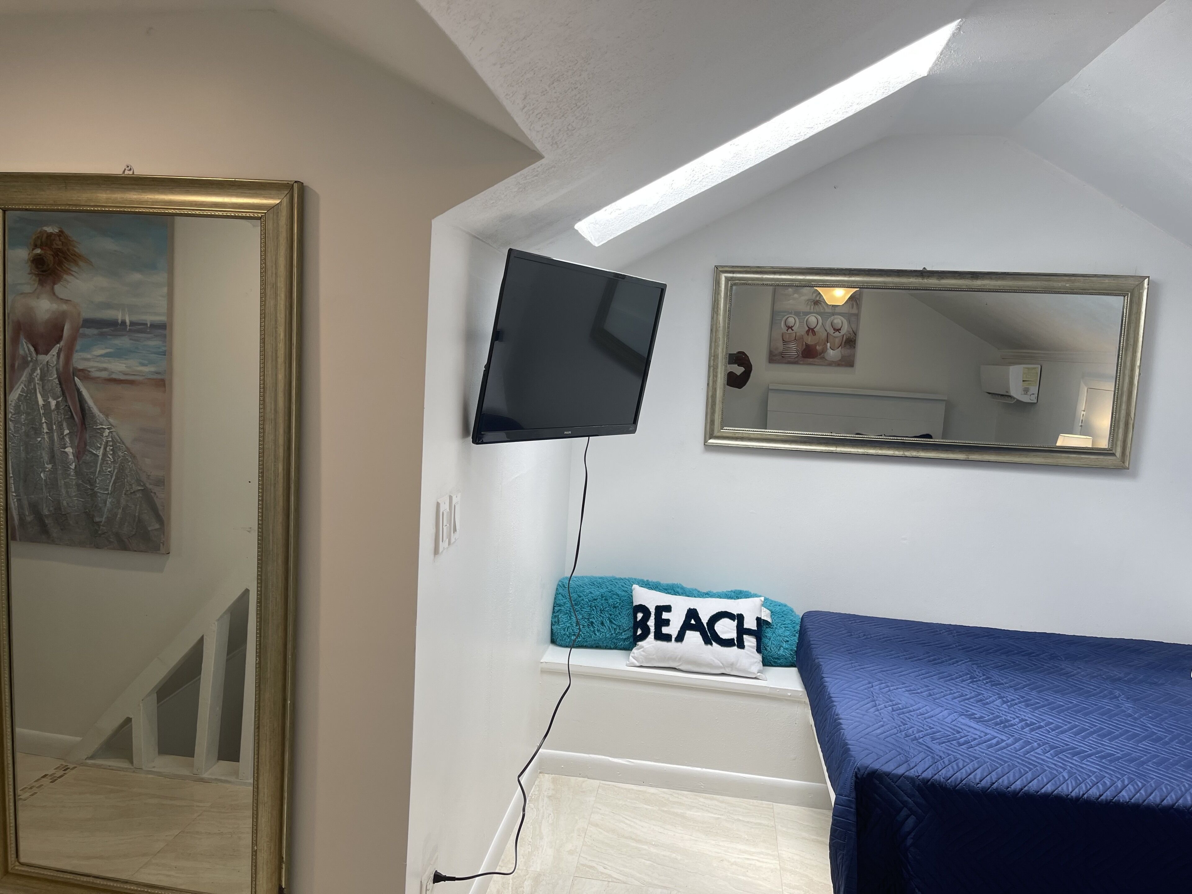 A bedroom with a bed, a TV mounted on the wall, a painting, and a mirror.