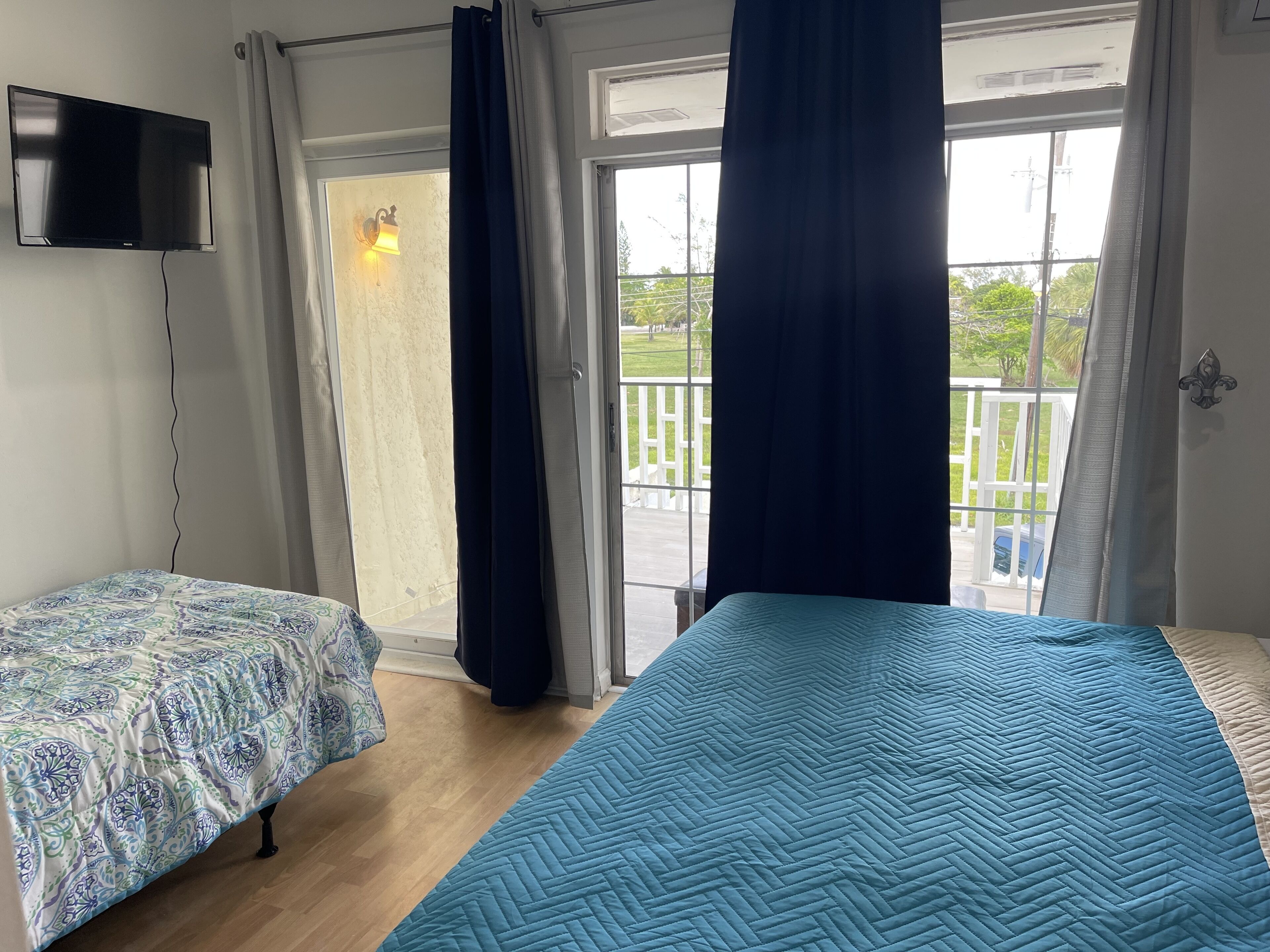 A room with a bed, a TV, and a balcony with curtains.