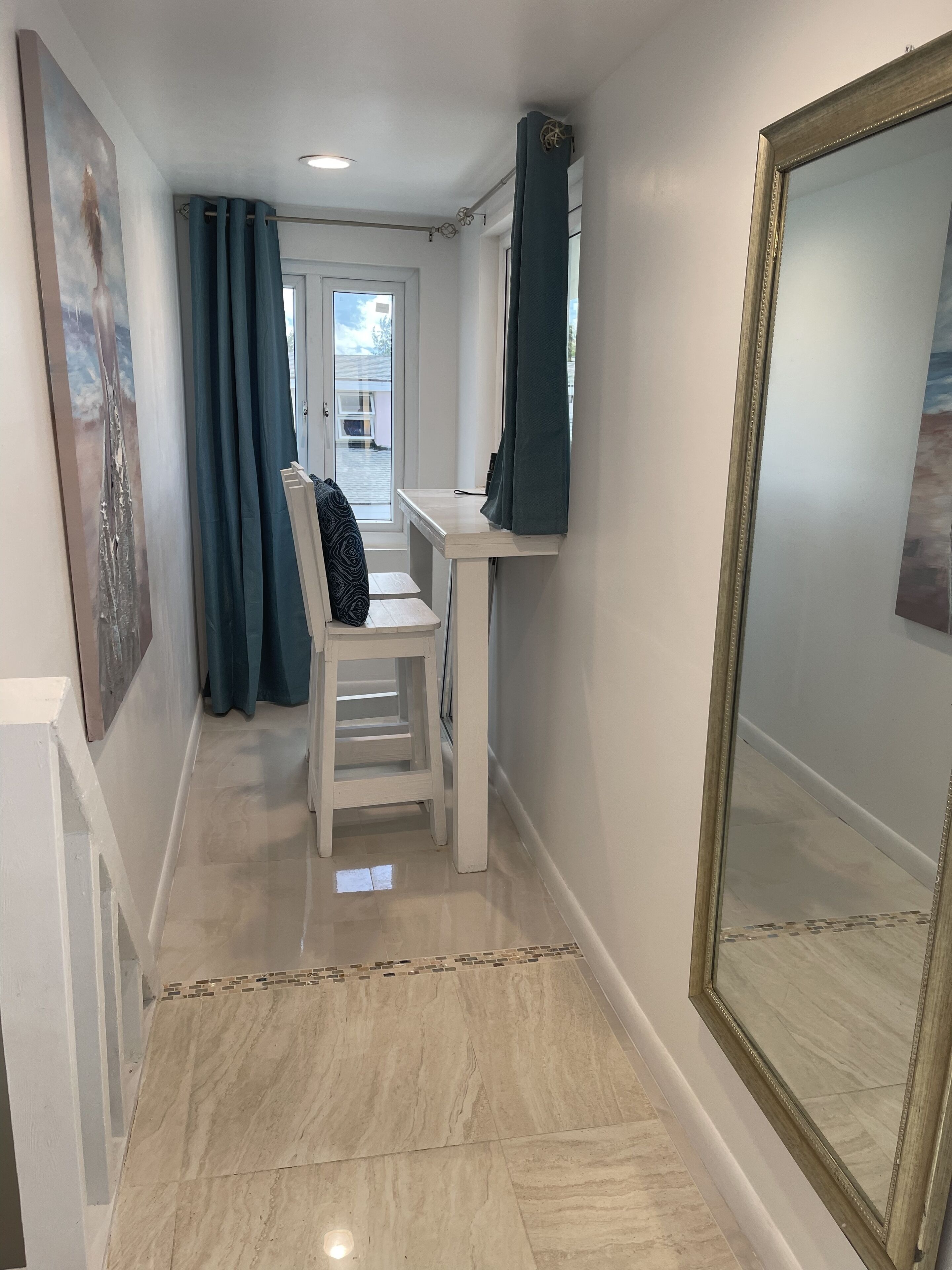 Un couloir avec une chaise blanche, un bureau et un grand miroir.