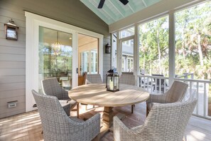 A covered patio with a round table and wicker chairs, a lantern, and a view of the outdoors.