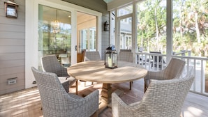 A covered patio with a round table and wicker chairs, a lantern, and a view of the outdoors.