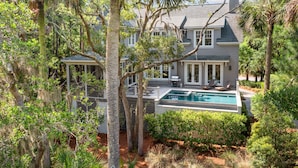 A large house with a swimming pool, surrounded by trees and greenery.