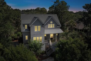 A two-story house with a covered porch, surrounded by dense trees.