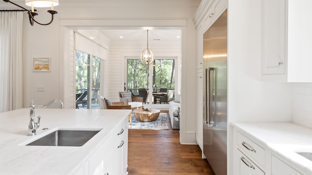 A modern kitchen with white cabinetry, a large island with a sink, and a dining area with a wooden table and chairs.