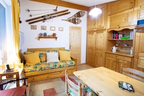 A cozy room with a wooden sofa, a table, and a shelf with books and a kettle.