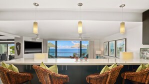 A modern kitchen with a large island, bar stools, pendant lights, and a view of the ocean.