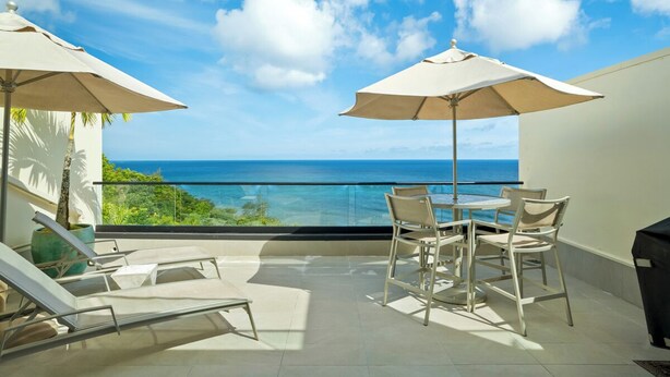 A balcony with a view of the ocean, a table with chairs, and two umbrellas.