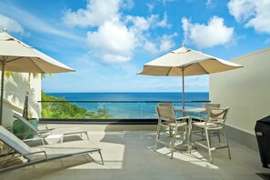Een balkon met uitzicht op de oceaan, een tafel met stoelen en twee parasols.