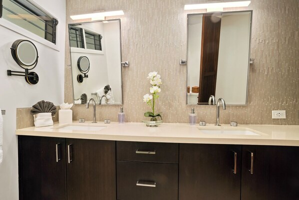 Een moderne badkamer met twee wasbakken, donkere kastjes en een spiegel met een ronde lijst.