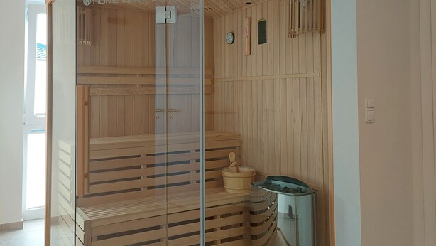 A corner sauna with wooden paneling, a glass door, and a bench inside. - NEW! modern, high-quality, central apartment, sauna, garden, wallbox in Burhave (Butjadingen)