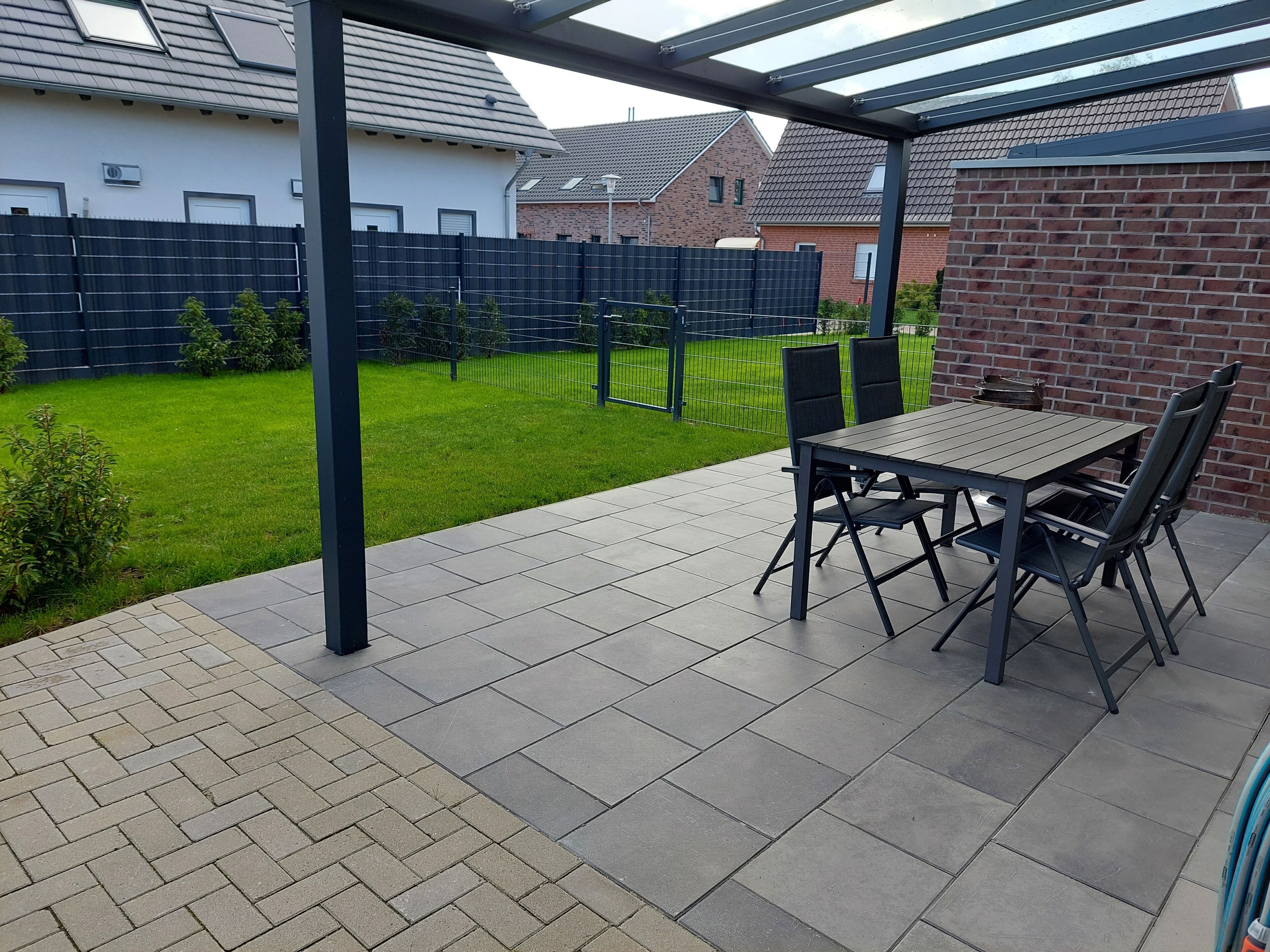 A covered patio with a table and chairs, a brick wall, and a green lawn.