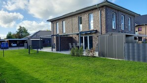 A two-story brick house with a covered patio and a fenced backyard. - NEW! modern, high-quality, central apartment, sauna, garden, wallbox in Burhave (Butjadingen)