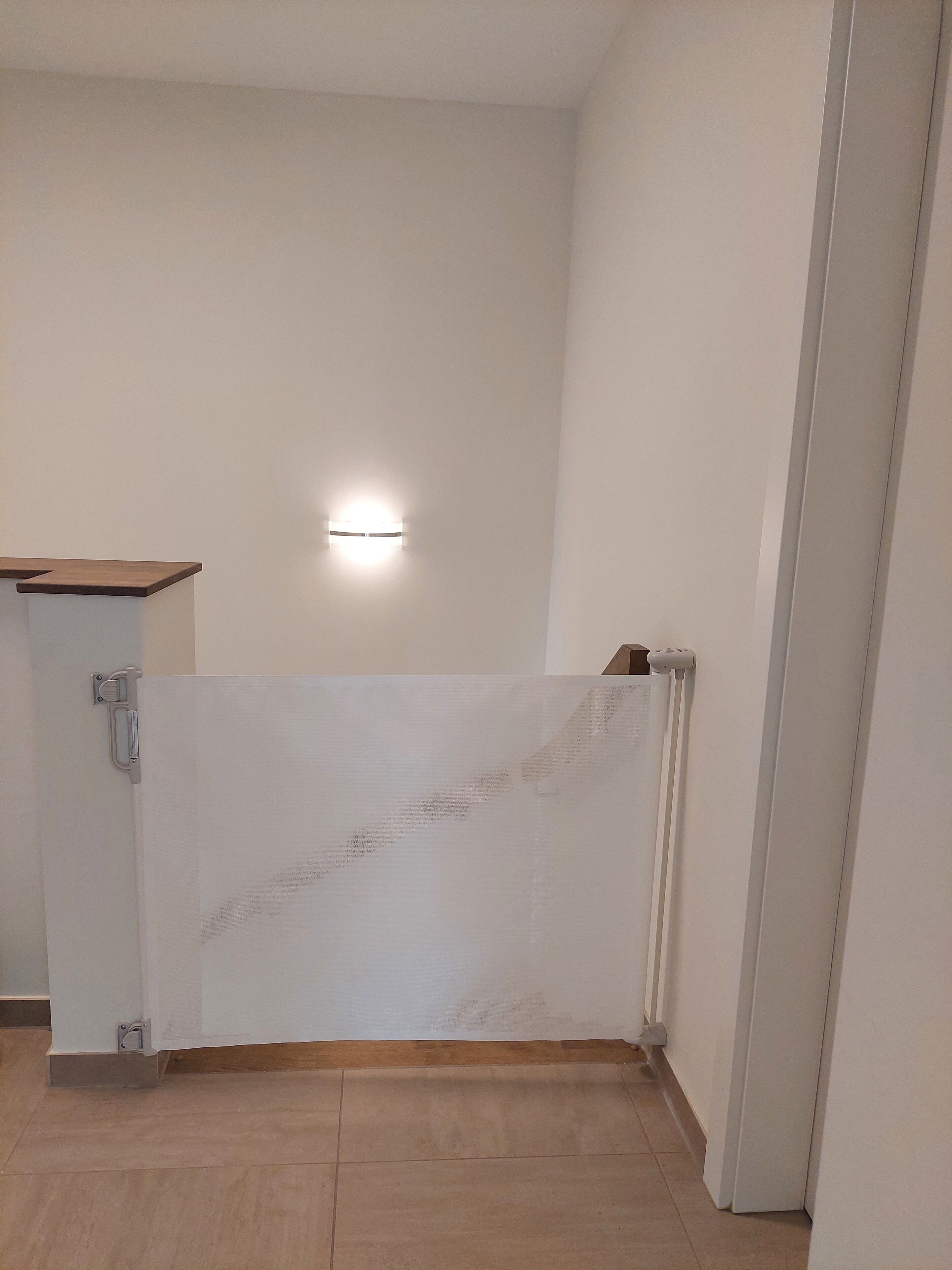 A room with a white wall, a wooden floor, a white door, and a light fixture.
