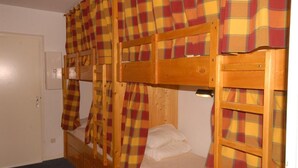 A bunk bed room with plaid curtains, a wooden headboard, and a small bedside table.