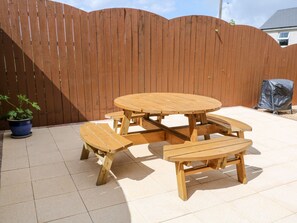 A wooden picnic table with benches, surrounded by a wooden fence, and a potted plant to the left.