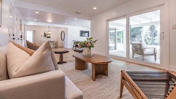 A modern living room with a sofa, coffee table, and a hammock. There is a large window with a view of the outdoors. - @ Marbella Lane - Cozy Modern Home w/ Relaxing Design & Pool (Fullerton)