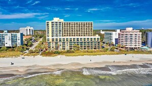 A beachfront hotel with multiple floors, a sandy beach in the foreground, and other buildings in the background. - Ocean front - 6th Floor Caravelle Resort (Myrtle Beach)